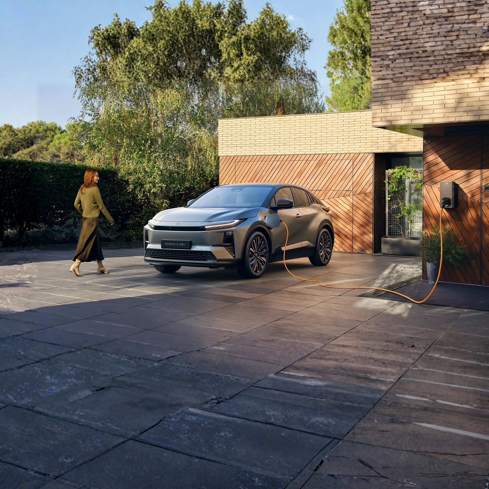 Auto Toyota C-HR+ parcheggiata davanti al garage di una casa moderna con una donna che sta per salirci sopra
