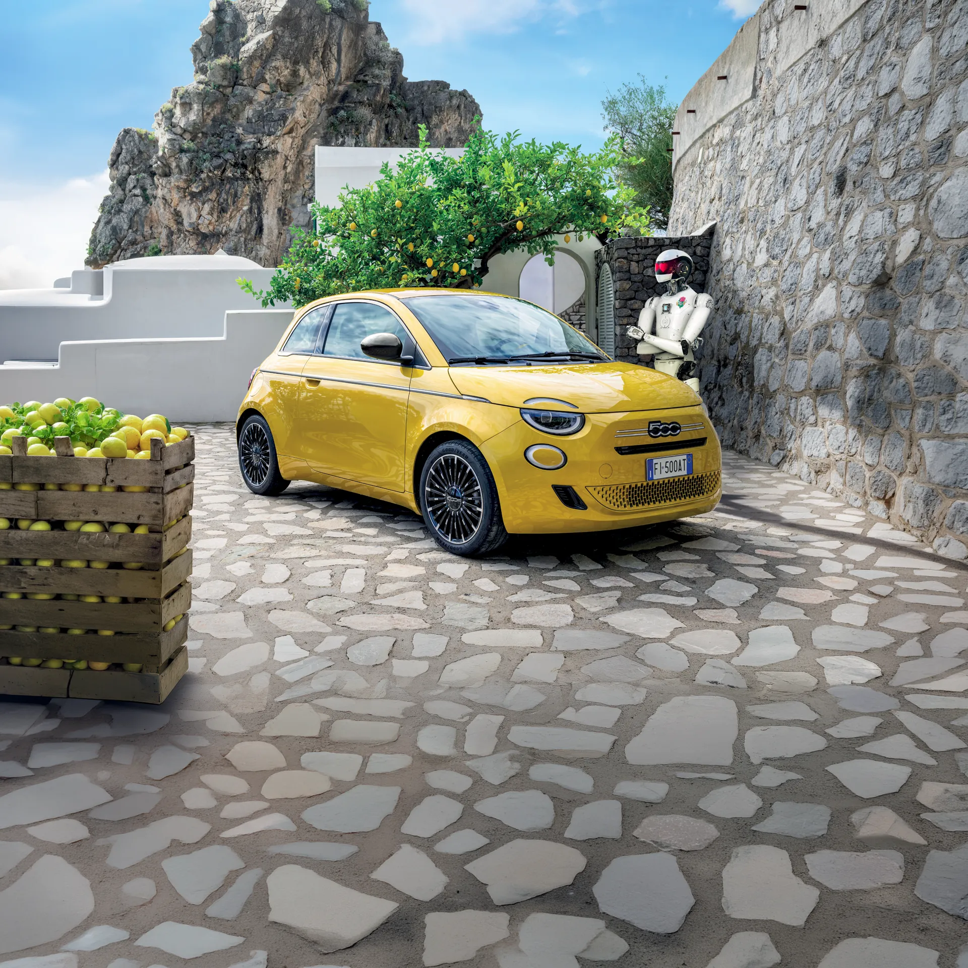 fiat 500 gialla parcheggiata in un piazzale di pietra con cassetta di limoni vicino e un robot